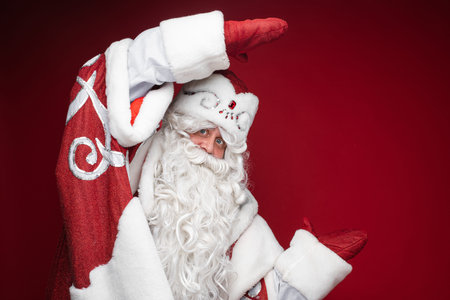 Happy Santa Claus shows size or dimension of discount by hands in mittens on red studio background with copy spaceの写真素材