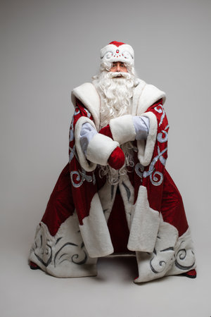 Cool gray haired with long beard Santa Claus in red clothes posing on gray studio backgroundの写真素材