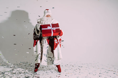 Santa jumping with Christmas present. Christmas present in hands under falling silver confetti.