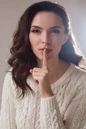 young caucasian model with long dark hair poses for the camera with hand near her face