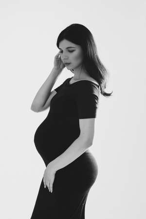 pretty caucasian pregnant woman in black dress and long hair posing for the camera in the studioの写真素材