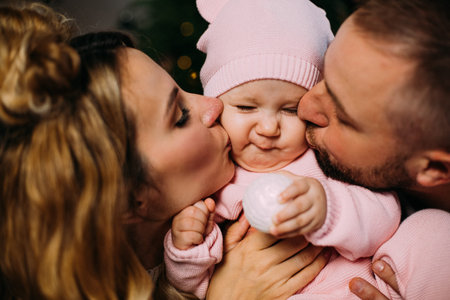 Young parents holding little daughter while kissing her together