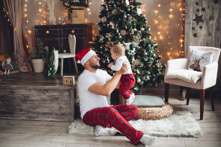Handsome young dad hold a baby near the christmas treeの写真素材