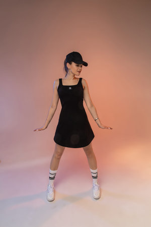 Stylish young girl female fashion model wearing sportive outfit, cool black sundress and cap posing in studioの写真素材