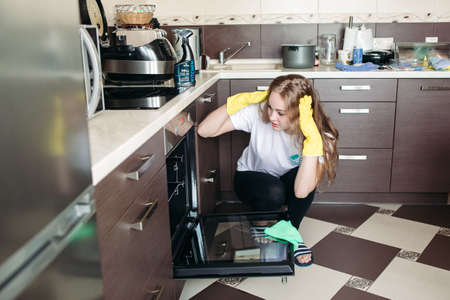 Woman in yellow protective gloves looking dirty oven at home kitchen.の写真素材