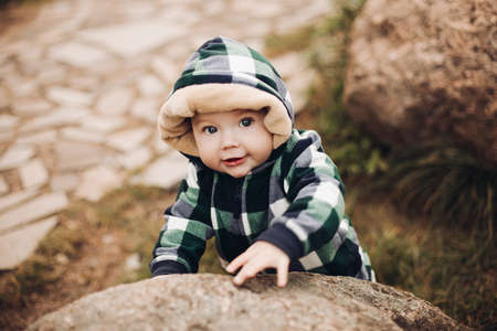 Adorable baby in warm overall with hood sitting on foliage.の写真素材