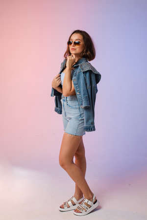 a woman in denim shorts, sunglasses in the studio on an interesting beautiful backgroundの写真素材