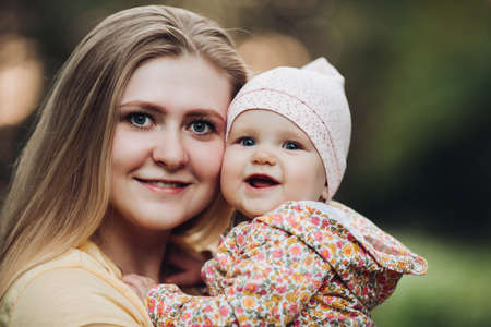 Beautiful mother and daughter walking in the park in autumn, portrait. Mom and daughter, family concept. A little girl in her mothers armsの写真素材