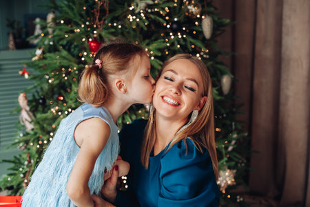 Little girl and her mom on Christmas morning at home. Girl is sad about something and mother is hugging her.の写真素材