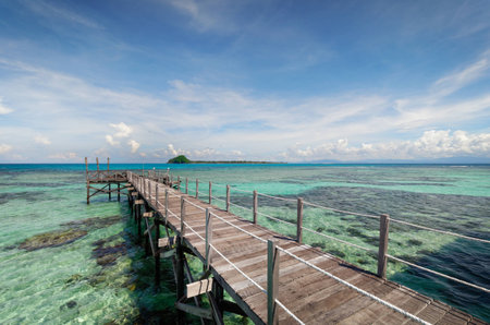 Rustic wooden pier extends into the ocean over clear water.の写真素材