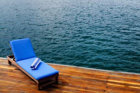 Outdoor reclining seat on deck next to lake. Matching blue and white towel rolled up on top.の写真素材