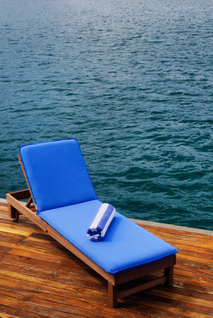 Outdoor reclining seat on deck next to lake. Matching blue and white towel rolled up on top.の写真素材