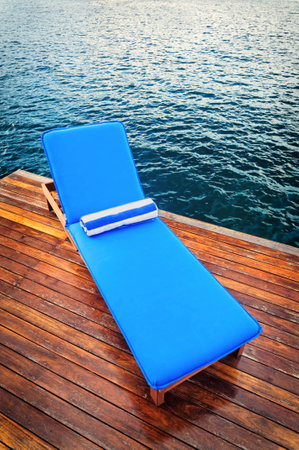 Outdoor reclining seat on deck next to lake. Matching blue and white towel rolled up on top.の写真素材