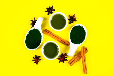 White spoon with spirulina powder on yellow background, cinnamon sticks and star aniseの写真素材