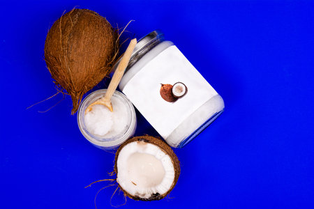 coconut oil in a jar with a wooden spoon and fresh coconuts, on a blue background
