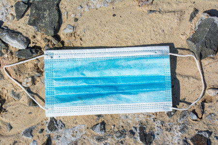 Blue surgical face mask lying on a dirt roadの写真素材