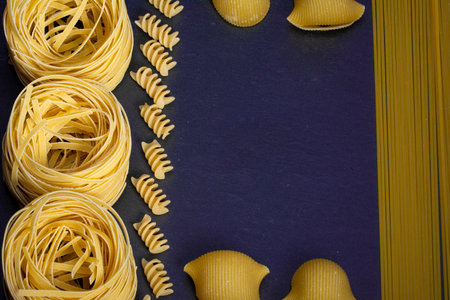 Assorted pasta wallpaper. Mix pasta, spaghetti, horns, spirals and seashells on blue background with copy spaceの写真素材