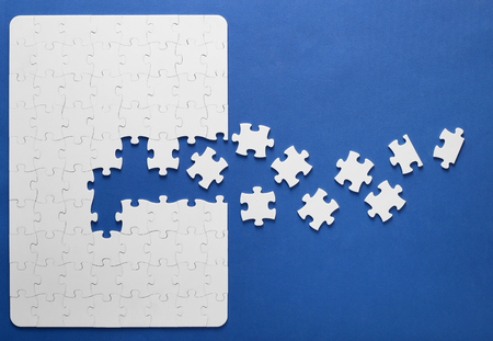 Collected white puzzles on a blue background with one missing piece close up. Symbol teamwork on the result.の写真素材