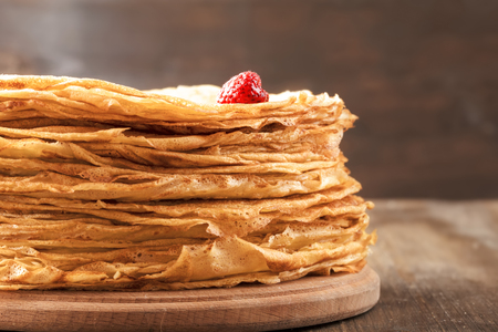 A pile of thin hot pancakes on a wooden surface close upの写真素材