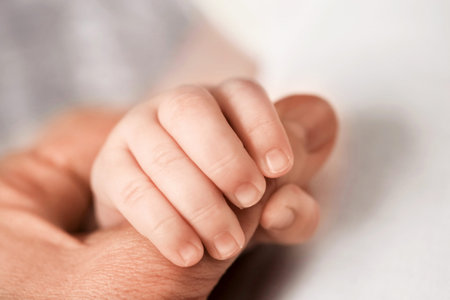 Little children's hand holds mom's finger. Care and love for the newborn.