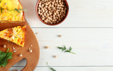 A slice of vegetarian pie made from chickpeas, spinach and lentils on a wooden table and a bowl of...