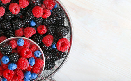 Blackberries, blueberries and raspberries with drops of water in a sieve close-up. Healthy fruits as...