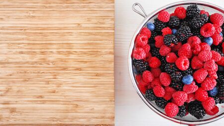 Blackberries, blueberries and raspberries with drops of water in a sieve close-up top view. Healthy fruits as an image of healthy eating copy spaceの写真素材