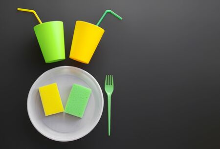 Disposable tableware on a dark background as a symbol. Using plastic dishes pollutes the environment. Plastic cup, plate and fork on a black background top view.の写真素材