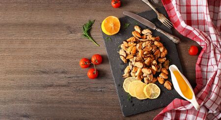 Ready peeled mussel on a stone board with lemon and salt top view. A wholesome seafood delicacy on a dark wooden table with place for text.の写真素材