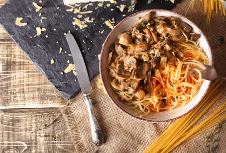 Cooked homemade pasta with mushrooms in a plate on a wooden surface top view. Vegan pasta dish with cheese and mushrooms.の写真素材