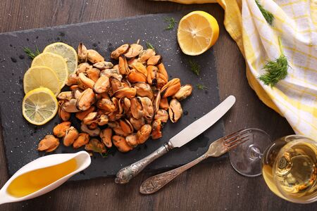 Ready mussel on a blue plate and board with seasoned butter and lemons on a dark wooden surface. Mussel delicacy top view.の写真素材