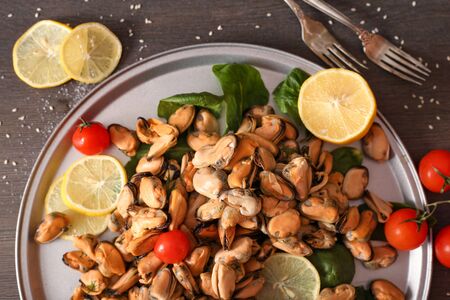 Ready mussel on a blue plate and board with seasoned butter and lemons on a dark wooden surface. Mussel delicacy top view.の写真素材