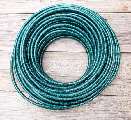 Water hose for irrigation is rolled into a ring. New long hose on an old wooden backgroundの写真素材