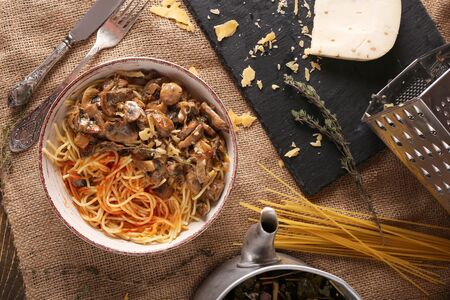 Cooked homemade pasta with mushrooms in a iron plate on a stone surface top view. Vegan pasta dish with cheese and mushrooms.の写真素材