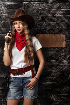 Beautiful sexy girl cowboy in a hat with a gun with place for text. Dangerous girl with a gun close-up. Brutal beautiful girl in the style of the Wild Westの写真素材