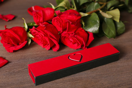 A bouquet of red roses and a gift in the form of a heart on a dark background top view. Bouquet of...