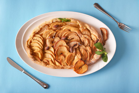 Traditional apple sliced fruit pie with honey, nuts, and mint top view. Taten apples and pears on blue background. Appetizing dessert, recipe and preparation of a pie with seasonal fruits.の写真素材