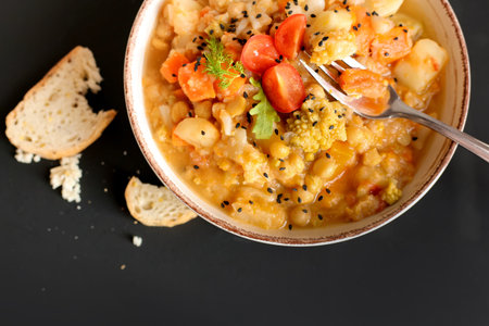 Vegetable vegan stew in a plate on a dark background top view with place for text. Healthy...