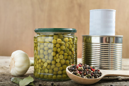 Glass jar of canned peas and iron cans of canned corn on wooden backgroundの写真素材