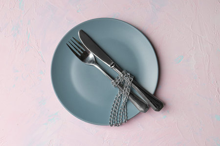 Gray plate on a pink background. Knife, fork, chain. The concept of diet and moderate nutrition. Starvation. Proper nutrition, menu. Food as a guarantee of health, choice of products and dishes.の写真素材