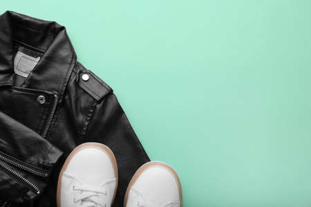 Children's leather jacket and white sneakers on a blue background. Female hand holds small baby shoesの写真素材