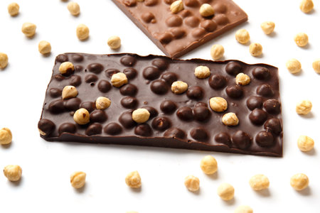 Bar of black and bar of handmade milk chocolate with hazelnuts and scattered nuts on a white background. Natural craft chocolate isolated.の写真素材