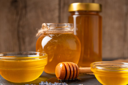 Honey in glass jars and bowls of different sizes and a wooden dipper lies in a drop of honey on a wooden background. The concept of natural organic honey.の写真素材