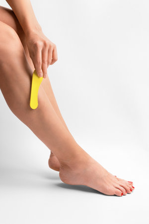 The girl does depilation of the legs in isolation. The girl's hand applies wax for depilation on the leg on a white background. Skin shugaring. body care. smooth legs.の写真素材
