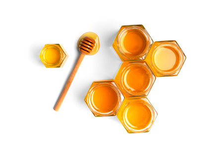 Creative composition of honey in open jars in the form of honeycombs and a wooden dipper on a white background top view. The concept of organic bee products. Honey on isolation.の写真素材