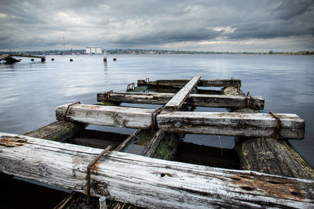 Old wooden pier on the river overlooking the city. A small destroyed bridge in the water.の写真素材