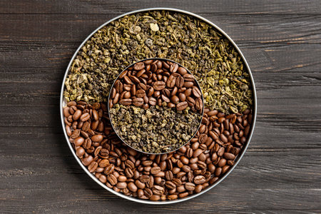 Green dry tea and coffee beans in two round plates of different sizes one on top of the other on a dark wooden background top view copy space. Conceptual composition of green tea and coffee beans.の写真素材