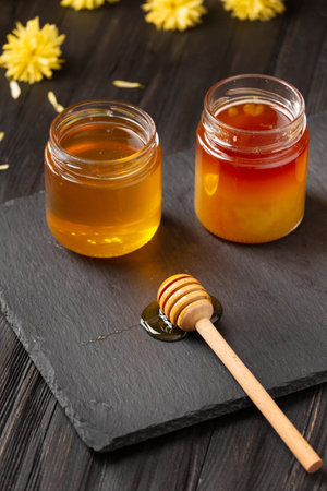 Honey in jars, dipper and flowers on a black stone plate on a wooden background. The concept of organic bee products.の写真素材