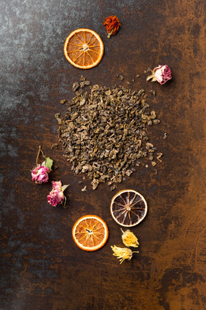 Green dry tea, flower tea and dry orange chips on brown background top view. Different types of tea and dry citrus slices on a dark background.の写真素材