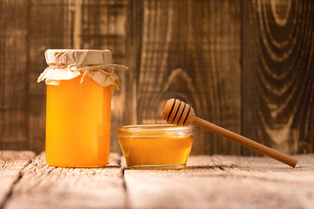 Creative composition of honey in a glass jar and a bowl, wooden dipper on an aged wooden background. The concept of organic bee products.の写真素材